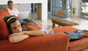 sad-girl-on-orange-couch-with-man-on-computer-in-background