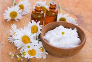 Beauty cream in bowl with chamomile on wooden background. Selective focus, horizontal.